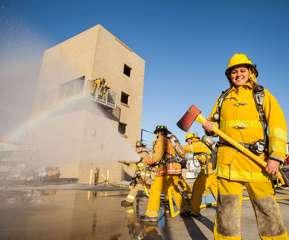 A fire cadet holds and ax and an another cadet sprays a firehose.