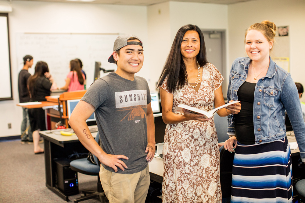 An instructor is holding an book open and two students are looking on.