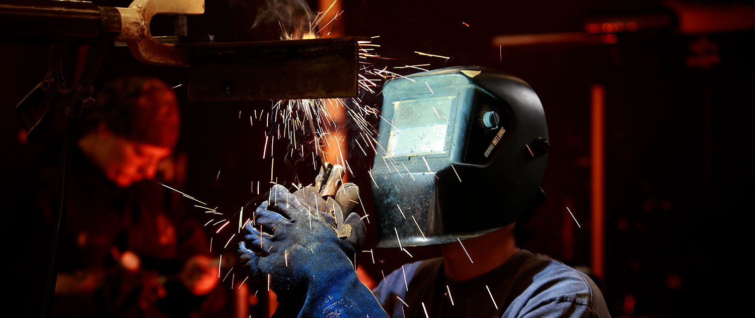 A welding student protects themself from sparks with a mask