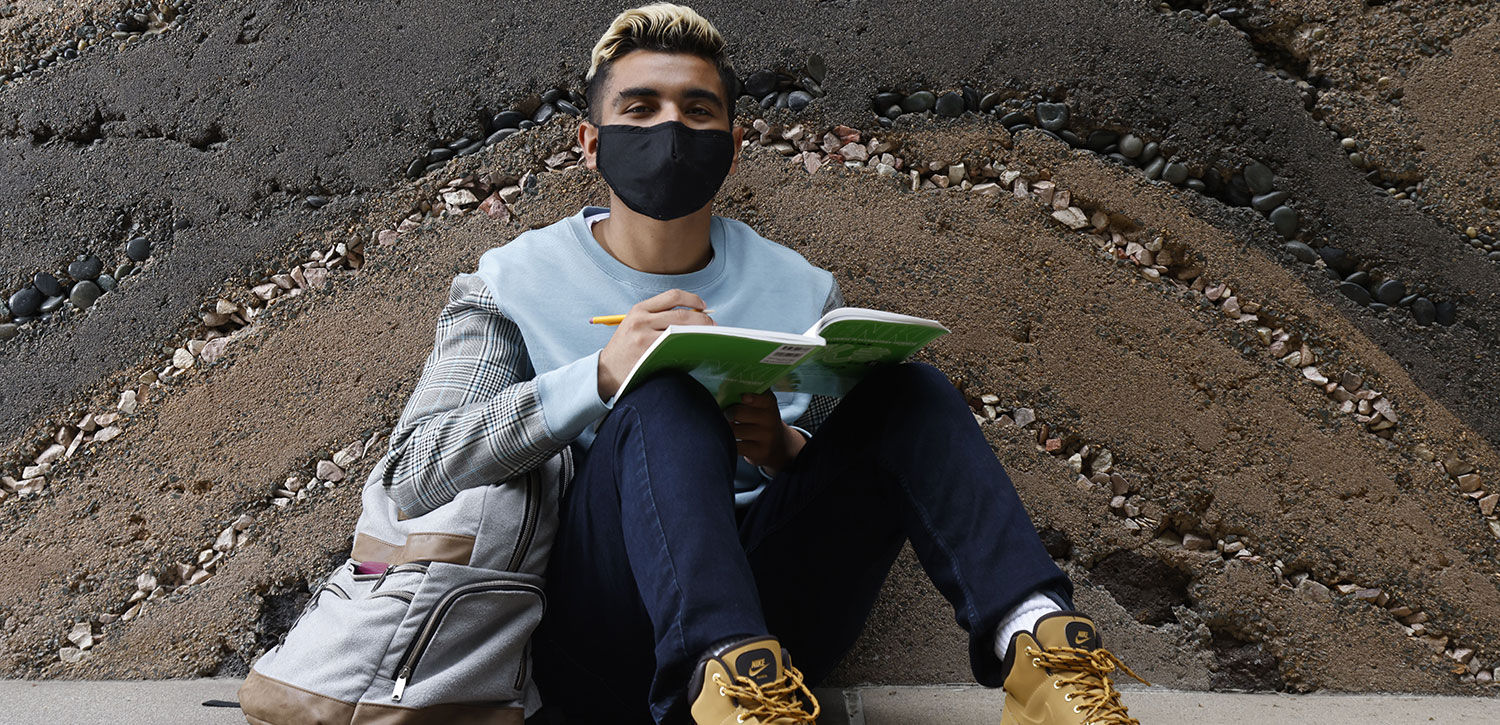 A student studies on campus while wearing a facemask