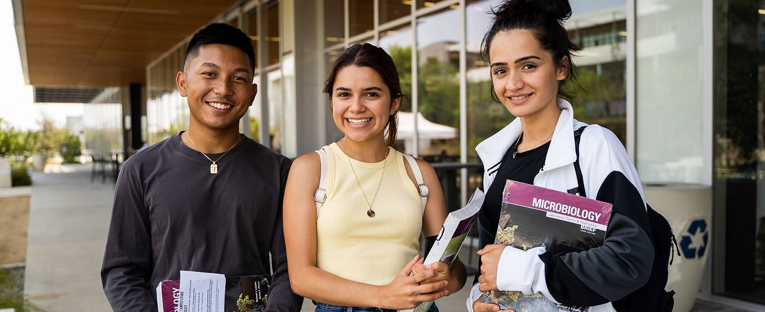 Three students hold books outside of Mesa Commons