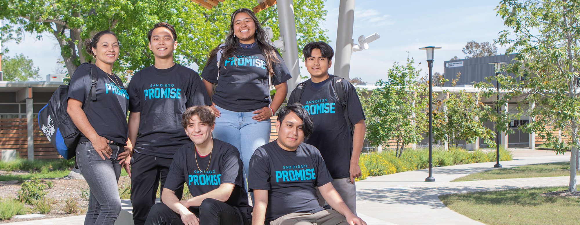 Six students wearing San Diego Promise t-shirts pose for a group photo outside on the grass in the Mesa Quad