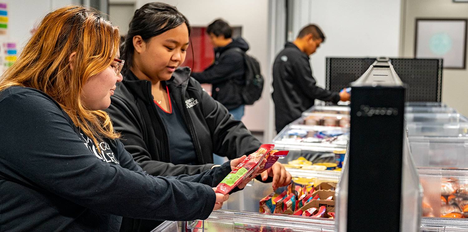 Two students look through bins of food at the food pantry.