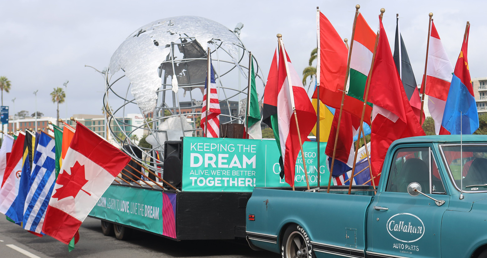 The parade float shows a metal spinning globe designed by welding students. There are several colorful flags from around the world surrounding the globe.