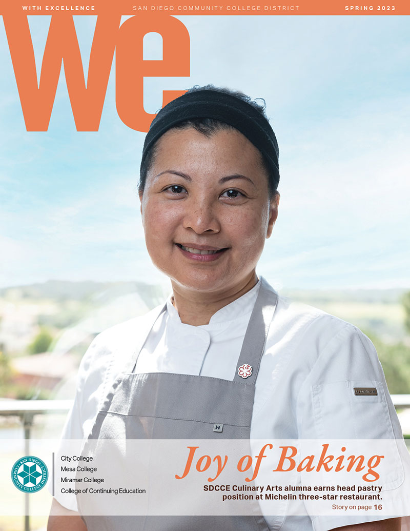 The Cover of Spring 2023 WE magazine. A woman is wearing a white chefs coat and a gray apron. Text reads the joy of baking