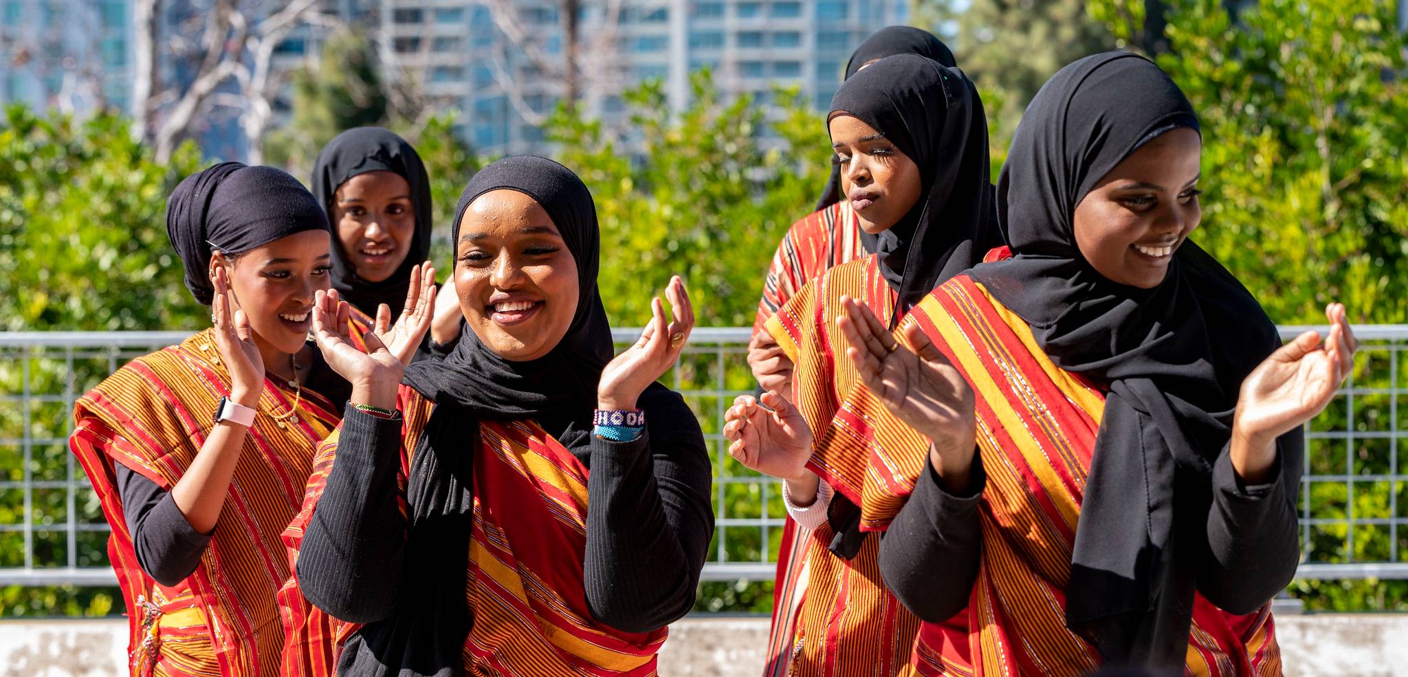 East African students wearing bright orange saris and black head scarves dance at a 2023 Black History Month event