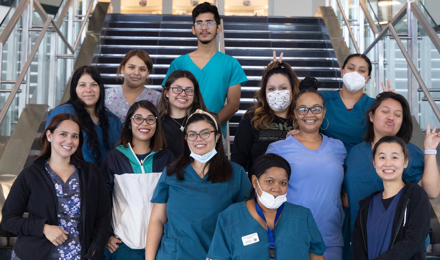 13 healthcare students in scrubs take a group photo on stairs