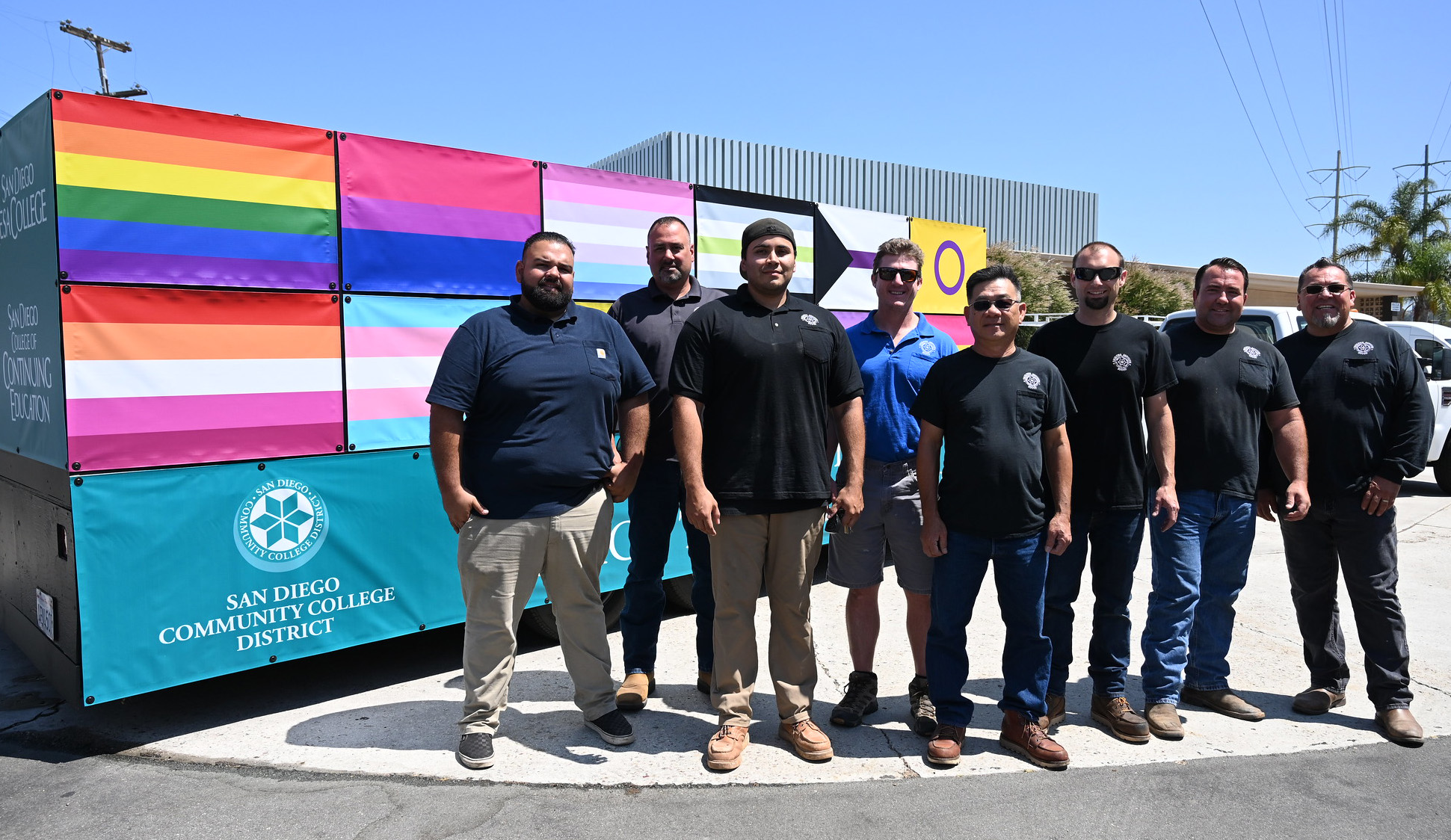 Eight facilities workers stand next to the pride float covered in various pride flags