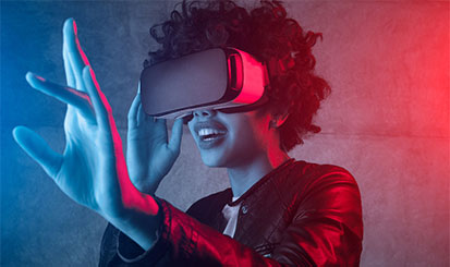A woman wears virtual reality goggles. She is lit up by a blue and red background