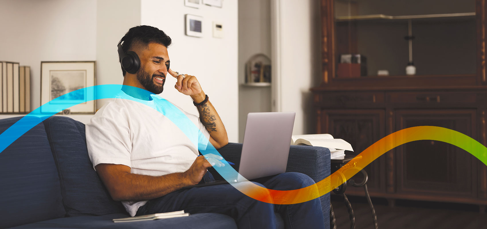 A student wearing headphones sitting on a couch looking at a laptop