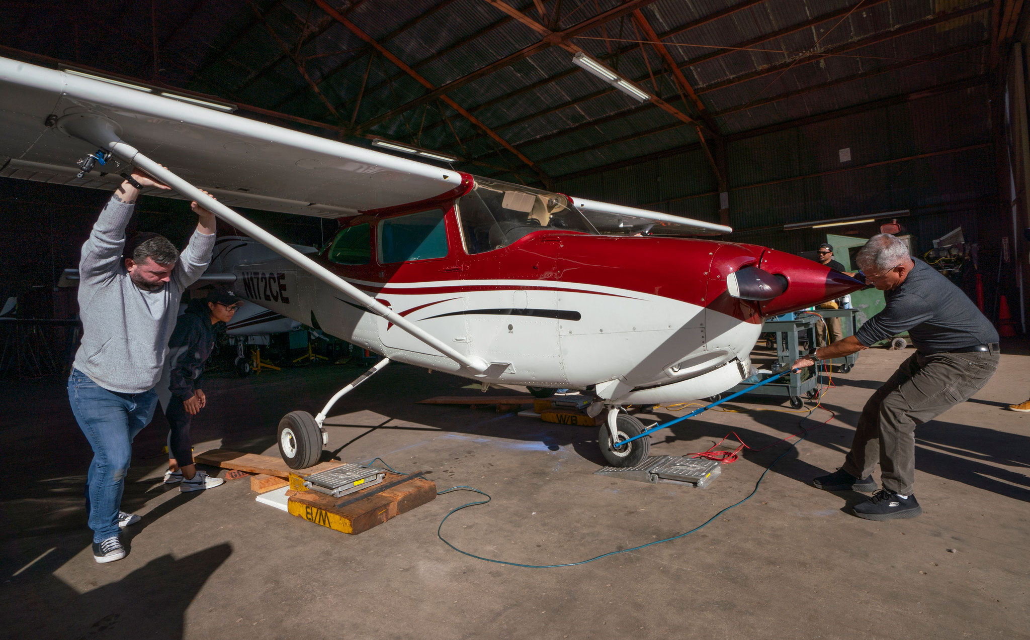 Two people push a small red and white plane out of a hangar