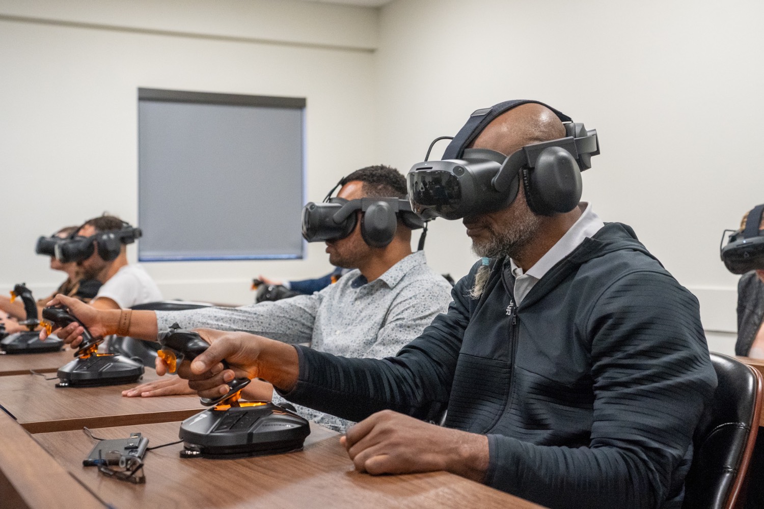People sitting at desks use virtual reality goggles and joysticks
