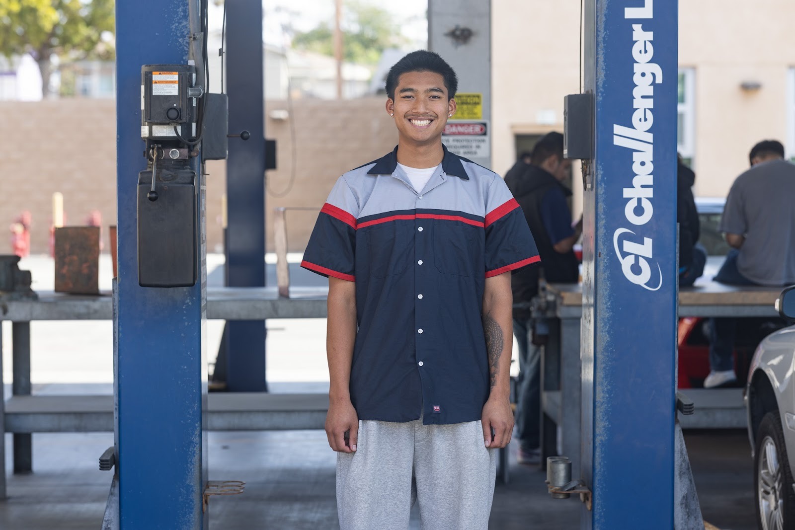 Jacob in a mechanic's bay wearing a blue and gray mechanic's shirt.