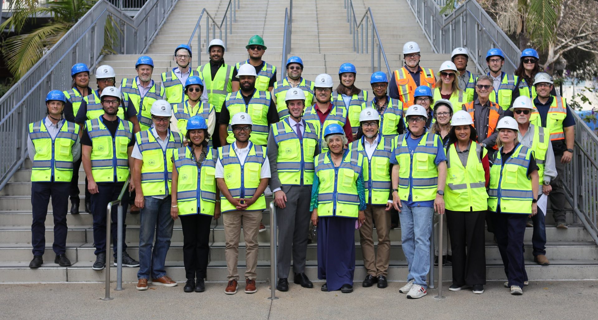 Group photo of Citizens’ Bond Oversight Committee members and Measure HH project team members wearing hard hats and safety vests on the steps outside a campus building