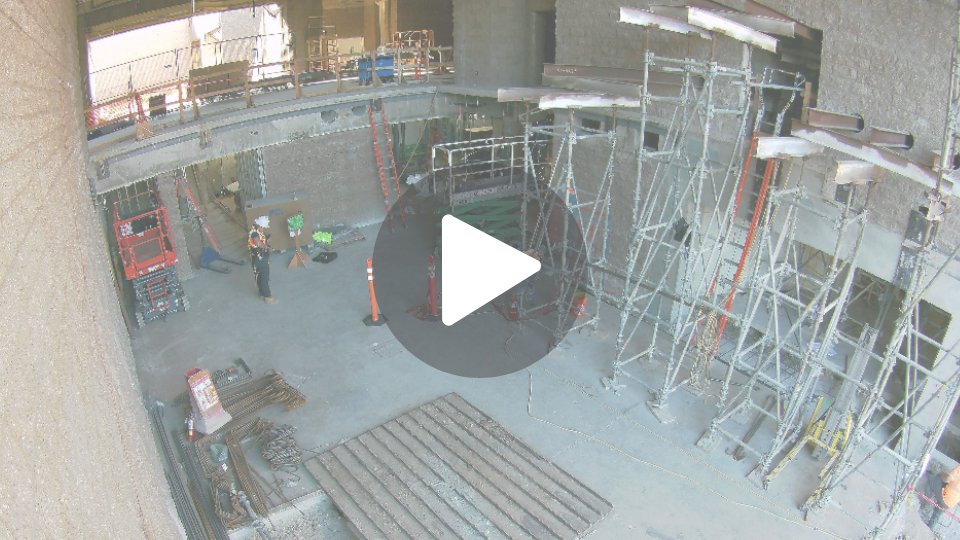 Construction site with scaffolding set up along a cement wall and many tools, storage, and safety barriers set up around the site. 