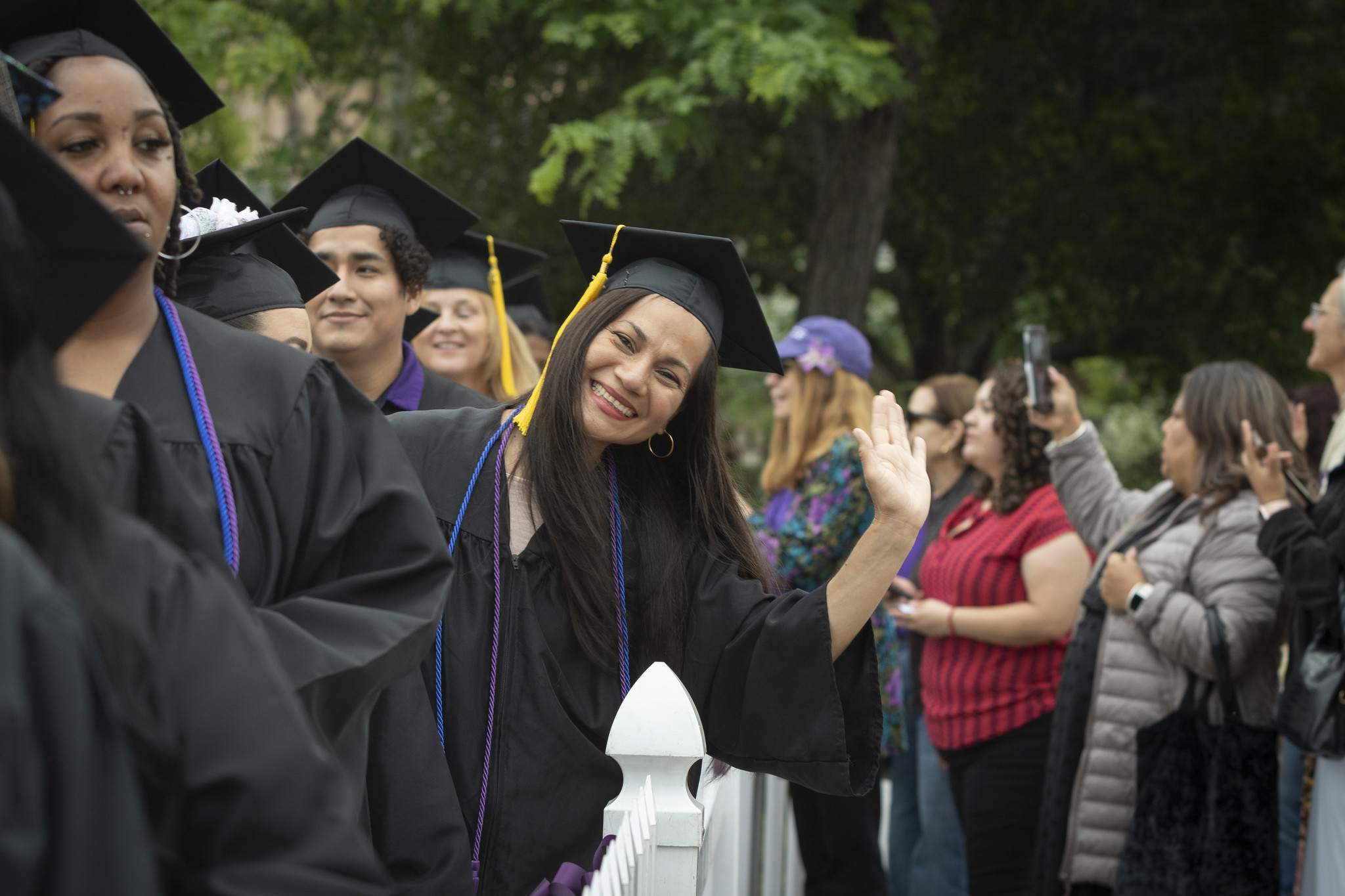 
A graduate in line leans over to wave to the camera.
