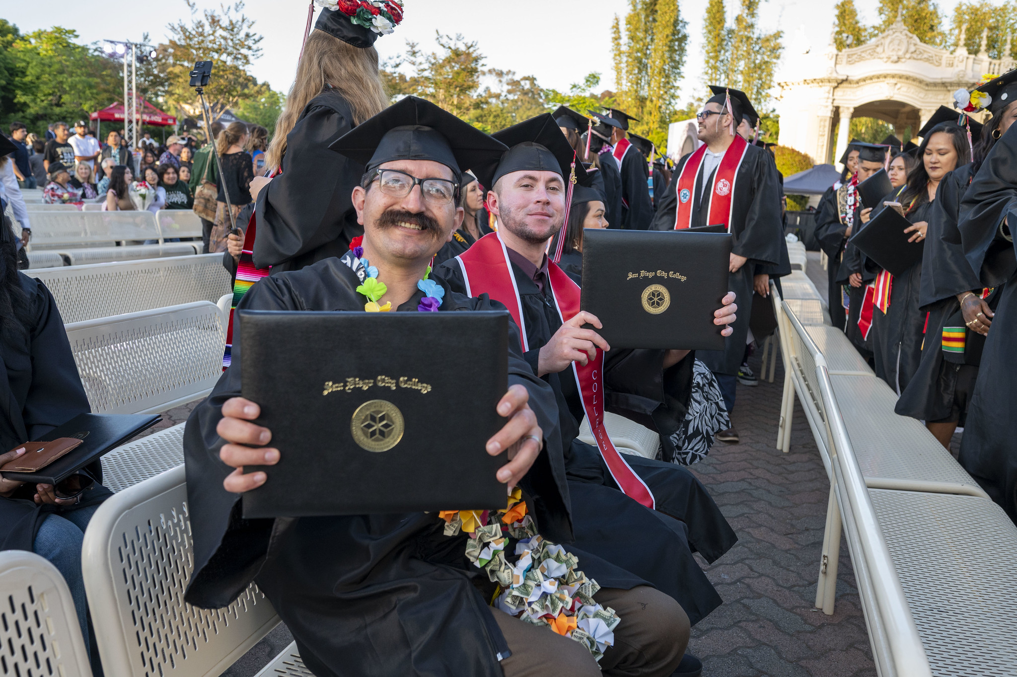 
Two grads in the audience hold up their degrees.

