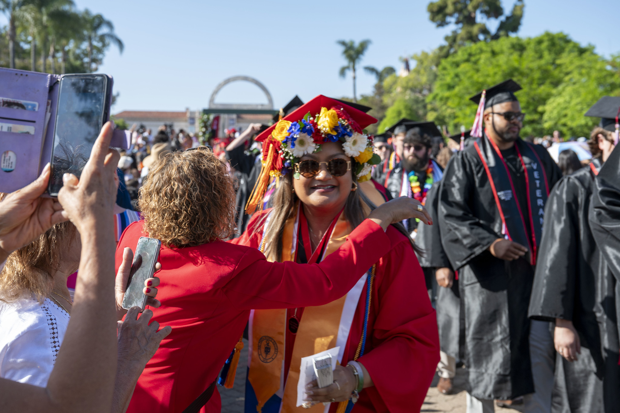 
A graduate with a red cap and gown with flowers in her hair.
