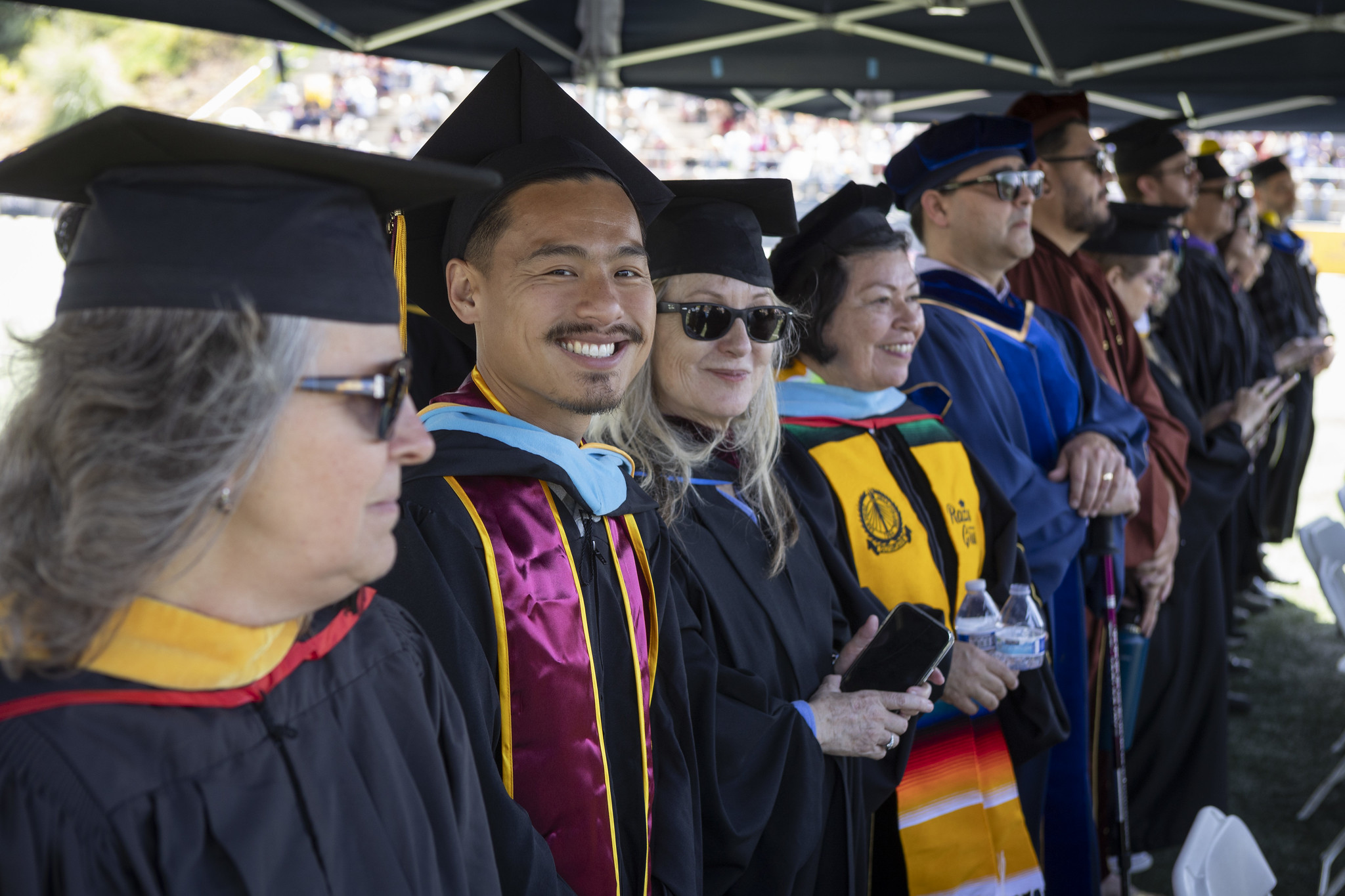 
A line of faculty and staff on stage cheer on the graduates.
