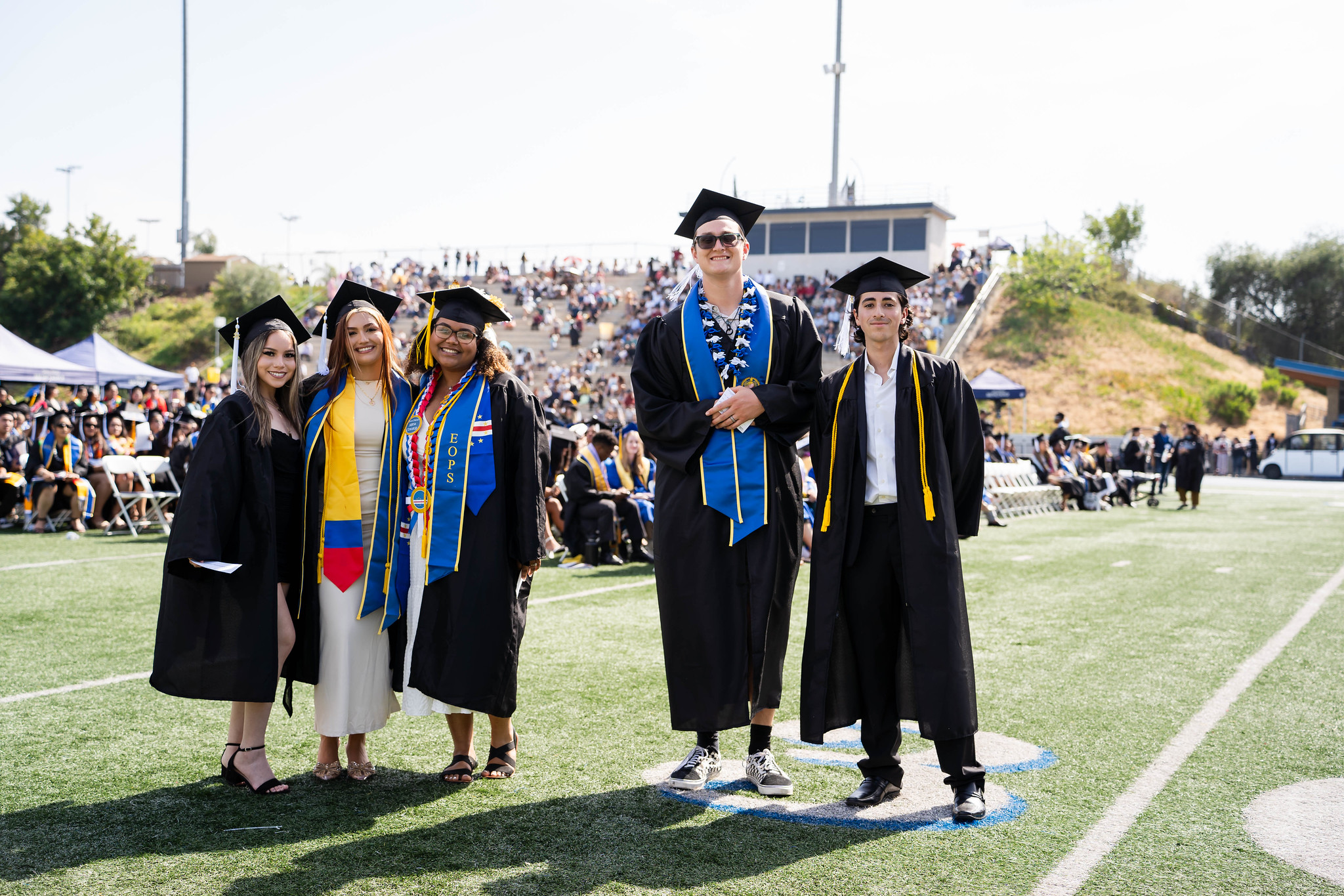 
Five graduates line up for a group photo on the field at commencement.

