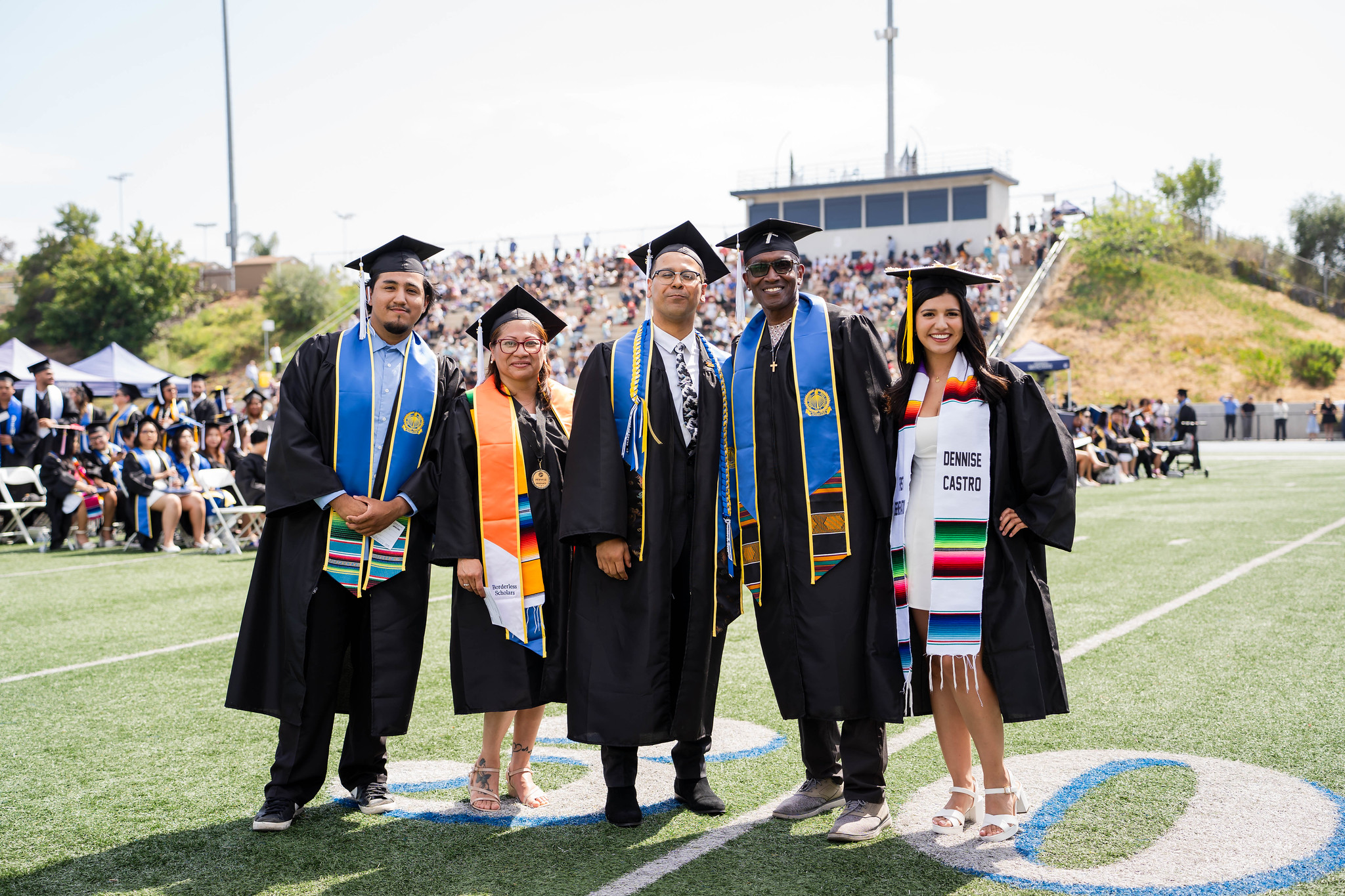 
Five graduates line up for a group photo on the field at commencement.
