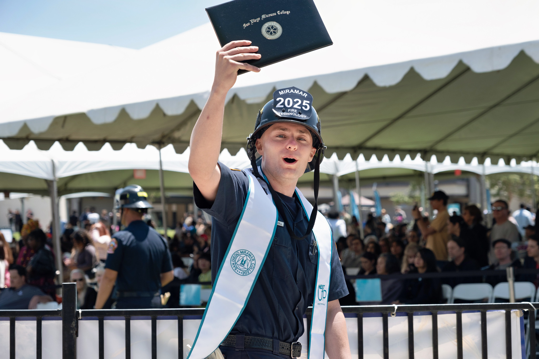 
A fire academy student in a black fire helmet holds up his degree.
