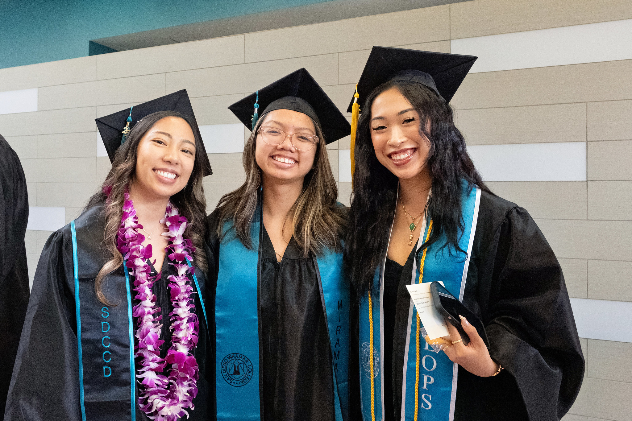 
Three graduates in black caps and gowns with teal sashes.
