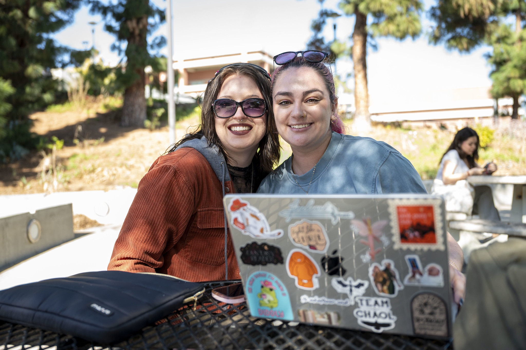 
Two women outsite seated at a table next to a laptop.
