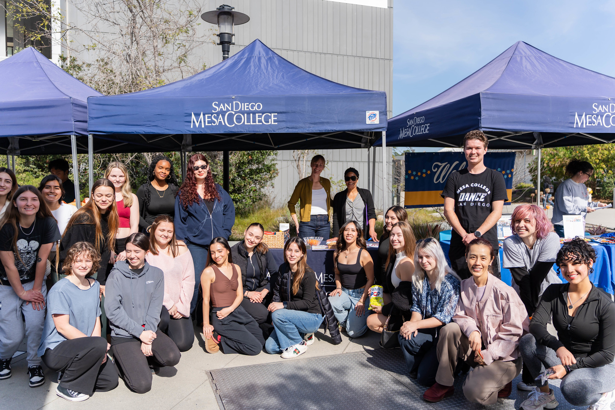
24 people take a group photo in front of a welcome tent.
